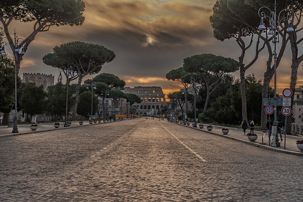 Empty road lined with trees, leading toward the Colosseum in Rome.