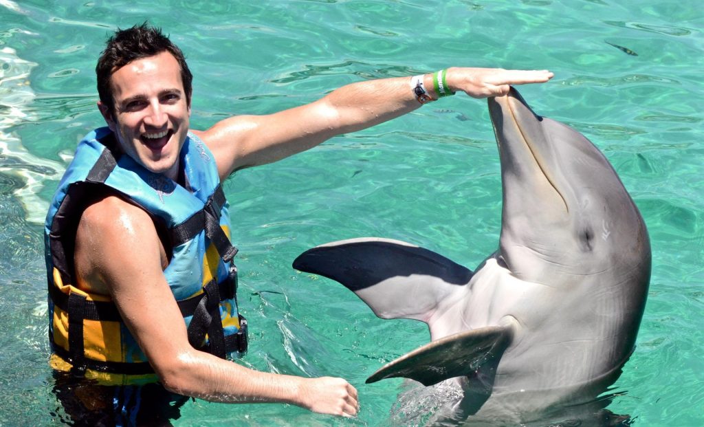 A joyful man extends his hand as a playful dolphin touches it with its nose during a Dolphin Encounter at Blue Lagoon Island in Nassau, Bahamas.