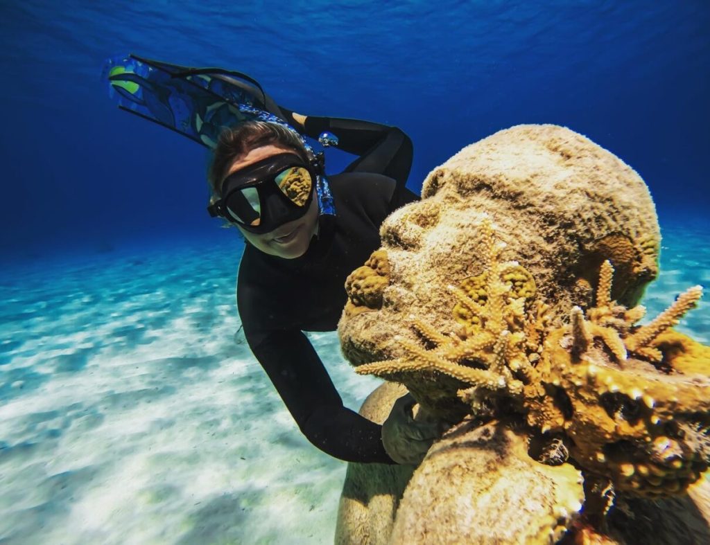 A female snorkeler explores a coral sculpture surrounded by marine life at Clifton Heritage Park in Nassau, Bahamas.