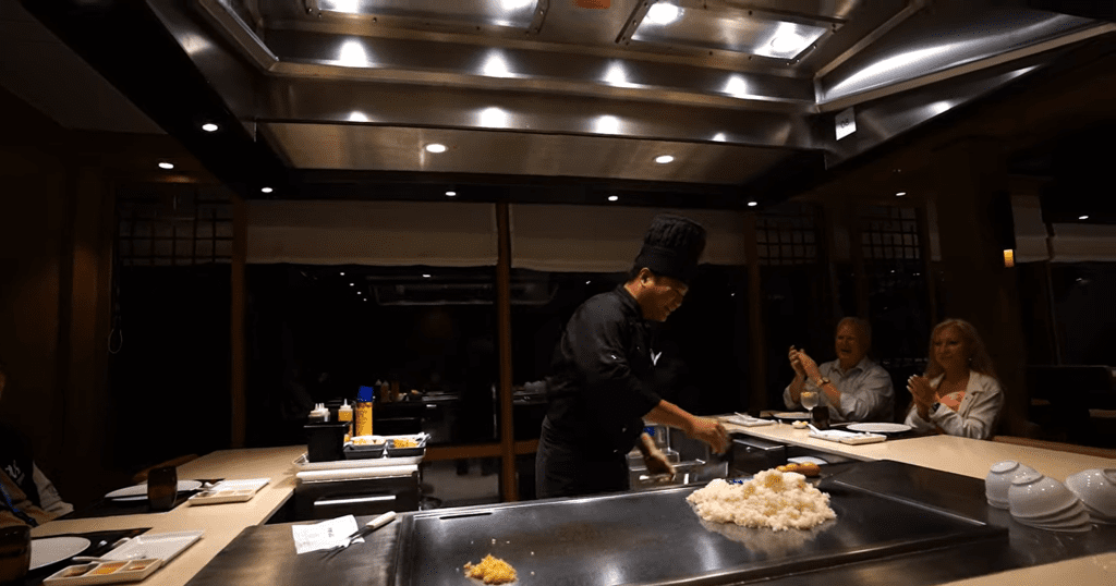 Teppanyaki chef preparing a meal on a hot grill in a Japanese restaurant.