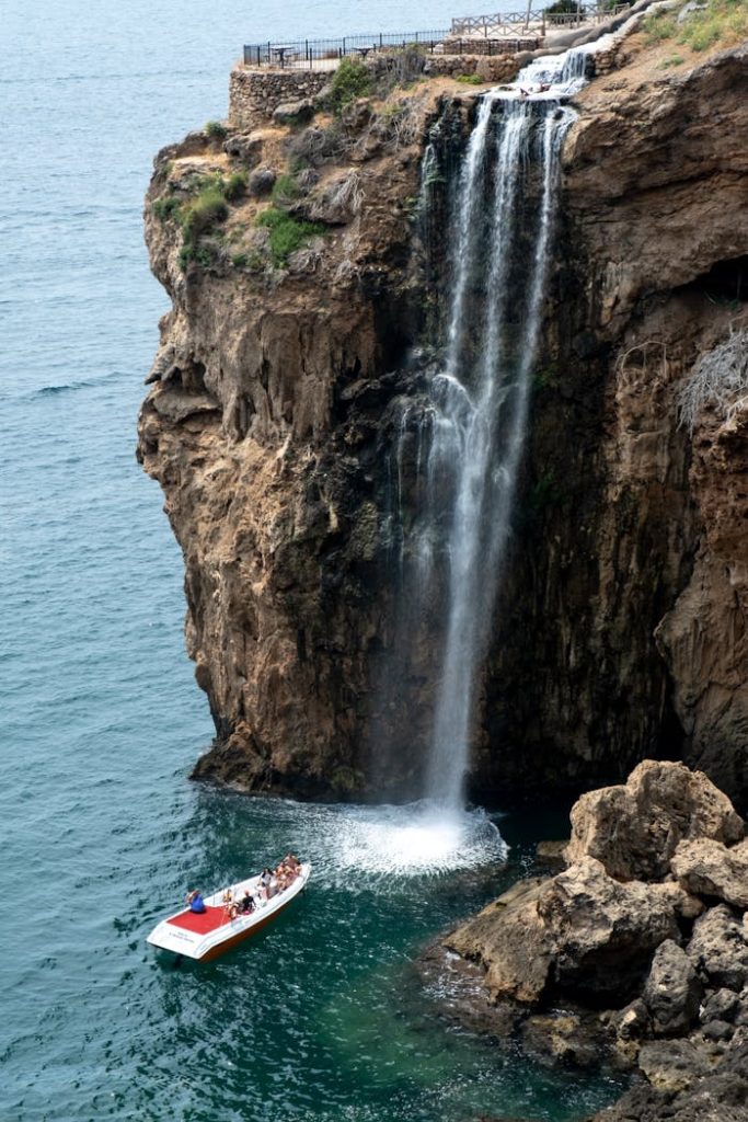 Dramatic waterfall cascading over cliffs in Antalya, Türkiye, with a boat nearby.