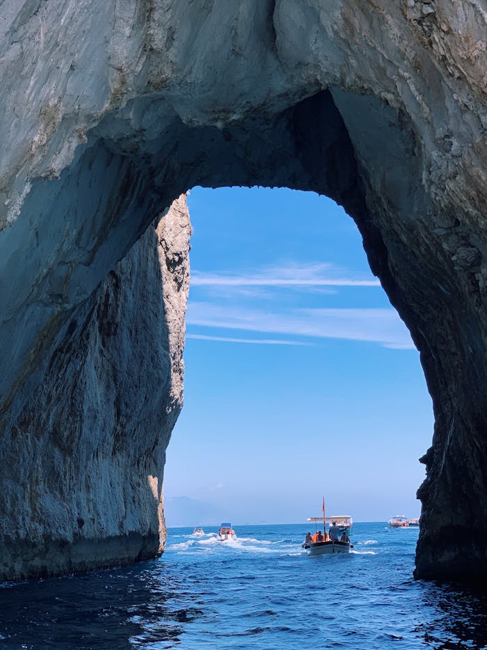 Scenic boats passing through natural archway on Amalfi Coast.